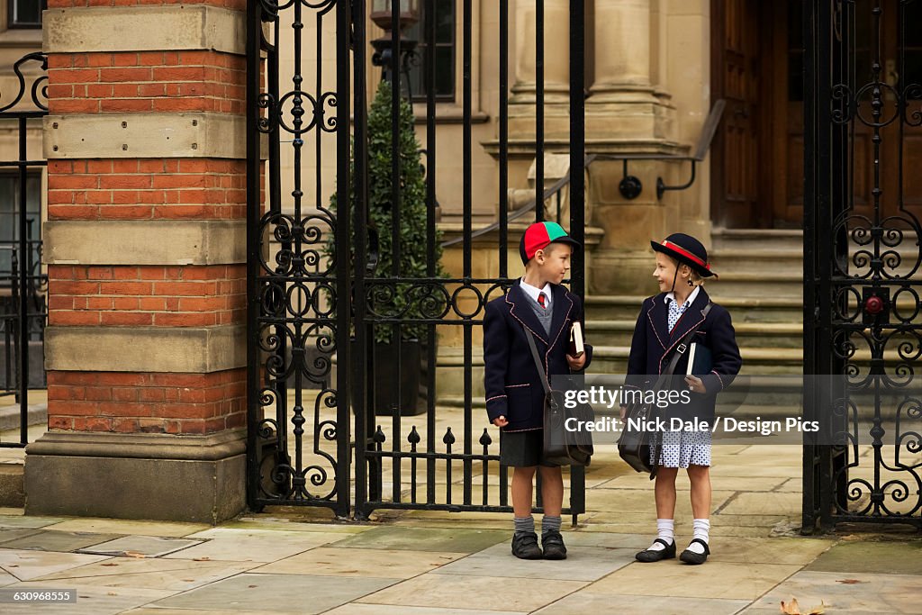 Young boy and girl students in uniform talking outside the school