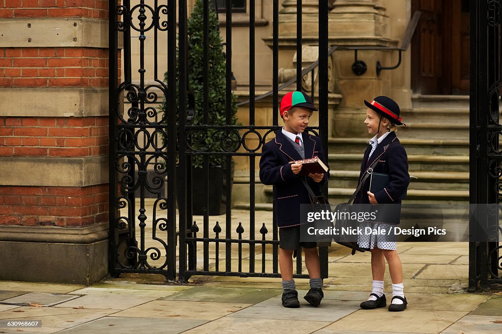 Young boy and girl students in uniform talking outside the school