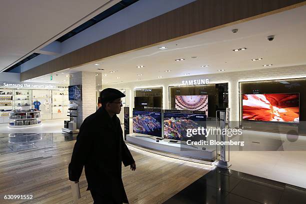 Man walks past Samsung Electronics Co. SUHD televisions displayed at the company's D'light flagship store in Seoul, South Korea, on Wednesday, Jan....