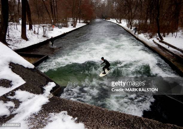 Surfers ride the Eisbach canal wave during freezing conditions on the Isar River in the English Garden in Munich, southern Germany on January 4,...