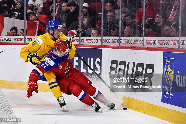 Gabriel Carlsson of Team Sweden forces Danil Yurtaikin of Team Russia into the boards as they skate after the puck during the 2017 IIHF World Junior...