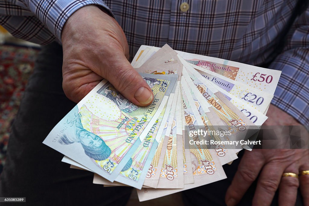 Pensioner holding British bank notes in right hand