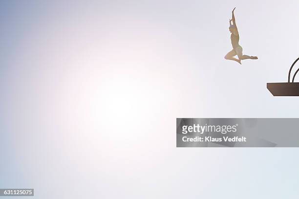 woman jumping from diving platform at sunset - courage photos et images de collection
