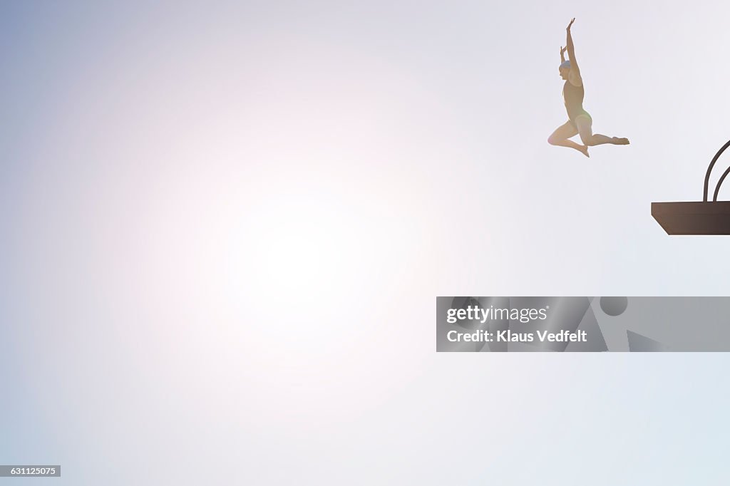 Woman jumping from diving platform at sunset