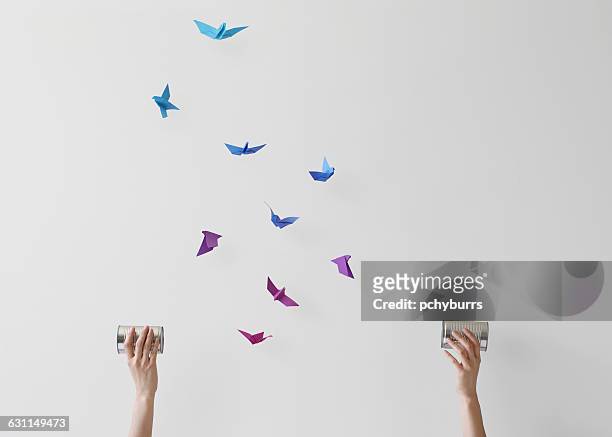 woman holding wireless tin can phones with conceptual birds flying mid air - representação de animal imagens e fotografias de stock