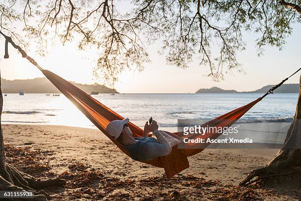 woman relaxes in hammock using smart phone - hammock phone stock pictures, royalty-free photos & images