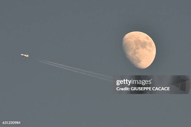 The moon appears in the sky as an aircraft flies past during the "Tour de Ski" Cross Country World Cup on January 8, 2017 in Cermis in the Italian...