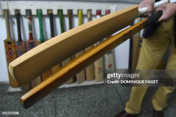 In this photograph taken on December 14 an Indian man holds old and new cricket bats in a factory in Meerut, some 70kms north-east of New Delhi. As...