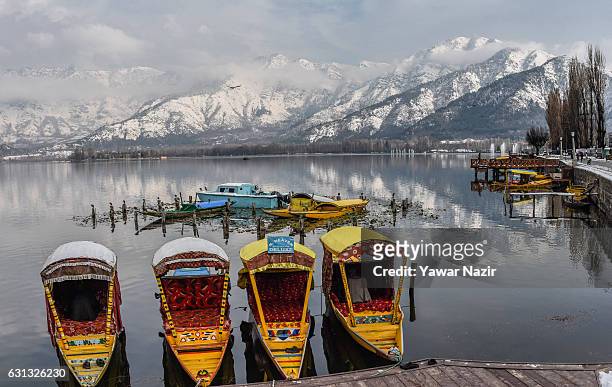 Shikara boats are moored to the bank as the snow capped Zabarvan mountain range is reflected on the waters of Dal Lake on January 09, 2017 in...