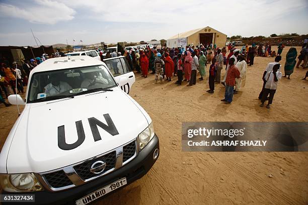 Sudanese refugees walk past a UN vehicle during a visit of senior officials from the United Kingdom to oversee a new cash assistance project...