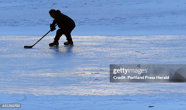 Sunset colors reflect off the frozen pond at Deering Oaks while Bo Hewey, of Portland, practices for an upcoming pond hockey tournament in Rangeley.