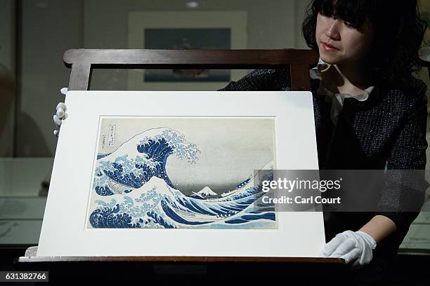 Curator poses for a photograph with a colour wood block print entitled 'The Great Wave off Kanagawa' during a press preview for an exhibition by...