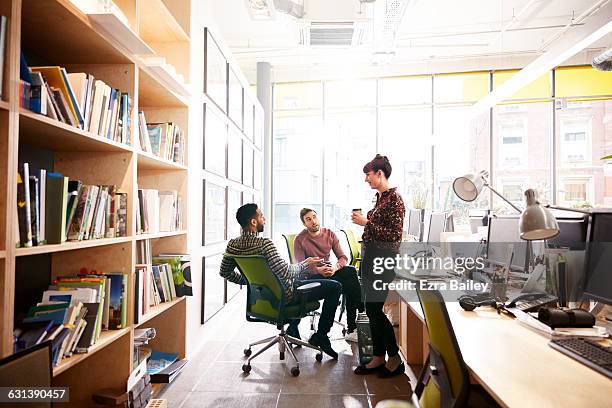 coworkers chat informally over coffee at desk - young women group stock pictures, royalty-free photos & images