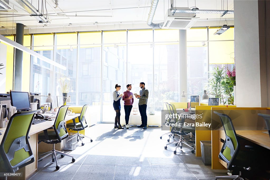Creative colleagues stand talking about ideas.