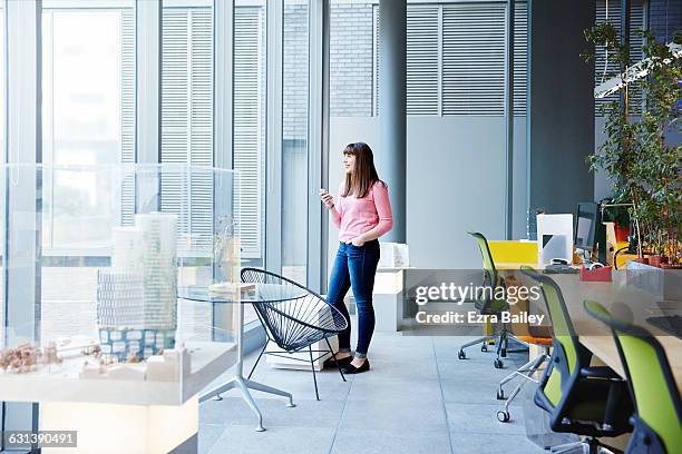 creative girl looking out of window holding phone - office desk top view stockfoto's en -beelden