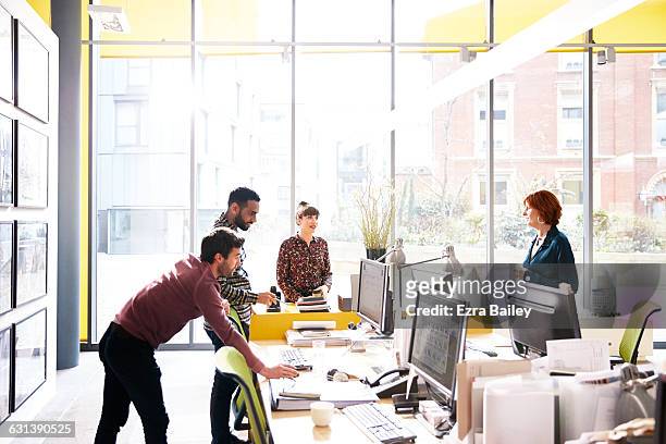 coworkers talking over ideas in open plan office - creative desk stock-fotos und bilder