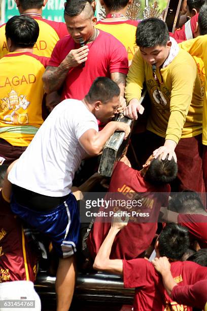 Devotee reverently kisses the cross of the miraculous Icon of the Black Nazarene as another devotee is given a blessing by an Hijo del Nazareno after...