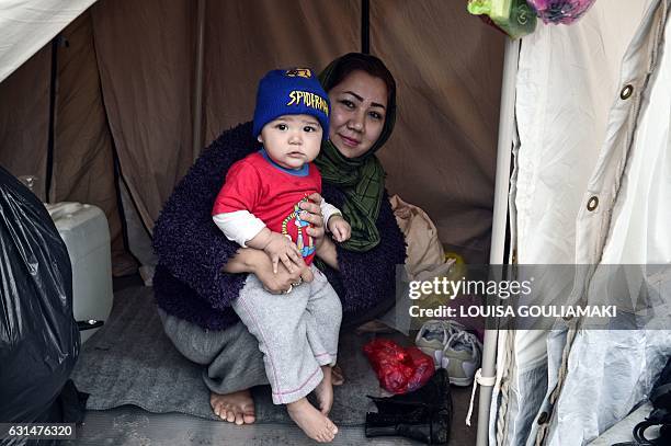 An Afghani refugee woman and mother of three poses with one of her children in their tent set up on a baseball field at a refugee camp in the...