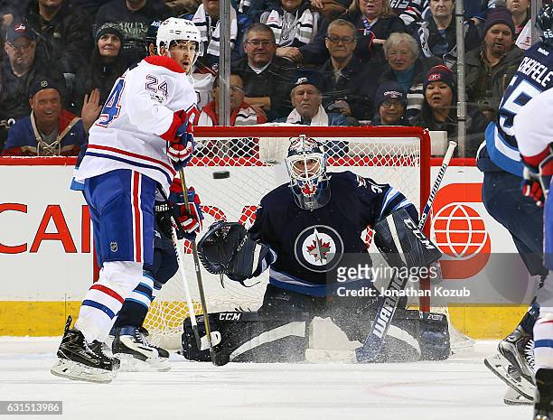 Phillip Danault of the Montreal Canadiens and goaltender Michael Hutchinson of the Winnipeg Jets keep an eye on the flying puck during second period...