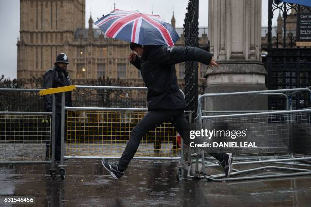 Pedestrian jumps over a puddle on the pavement outside the Houses of Parliament in central London on January 12, 2017. Severe weather warnings were...