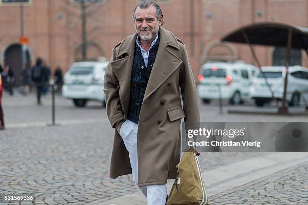 Alessandro Squarzi is wearing a brown wool coat, denim jacket, white pants on January 12, 2017 in Florence, Italy.