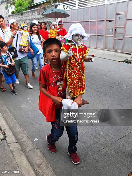 Young boy in red outfit carrying a Santo Niño. The Santo Niño symbolizes the whole mystery of the childhood of Jesus Christ. The Catholic Church of...