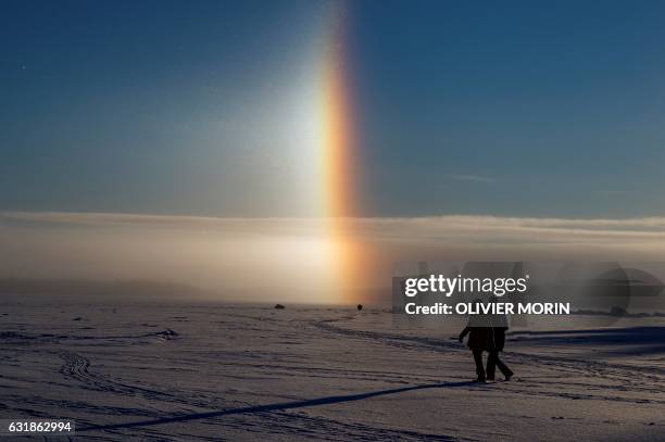 People walk near a solar halo on the frozen sea in Vaasa by -15°C, on January 15, 2017. - The Halo is an optical phenomena produced by light...