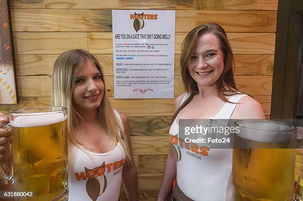 Hooters Girls; Yana Aerts and Hailey Sprenger hold beers in front of the Angel shot poster at Hooters Restaurant on January 16, 2017 in Johannesburg,...