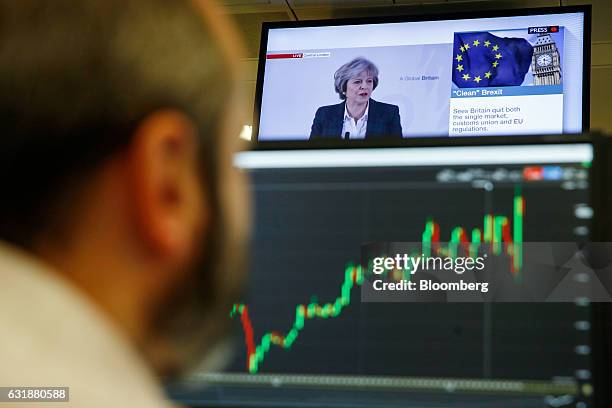 Television screen displays a news channel showing U.K. Prime Minister Theresa May making her Brexit speech, as a trader monitors financial data on...