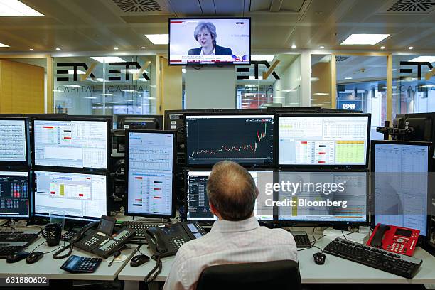 Television screen displays a news channel showing U.K. Prime Minister Theresa May making her Brexit speech, as a broker monitors financial data on...