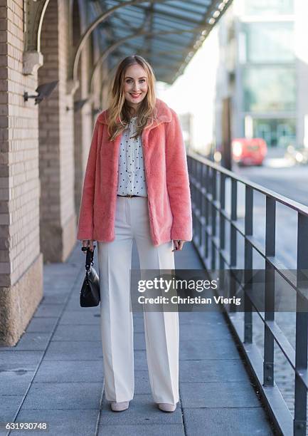 Sandra Kleine Staarman wearing a salmon pink Marc Cain faux fur jacket, white wide leg Marc Cain pants, and Marc Cain blouse with bow tie, black Marc...