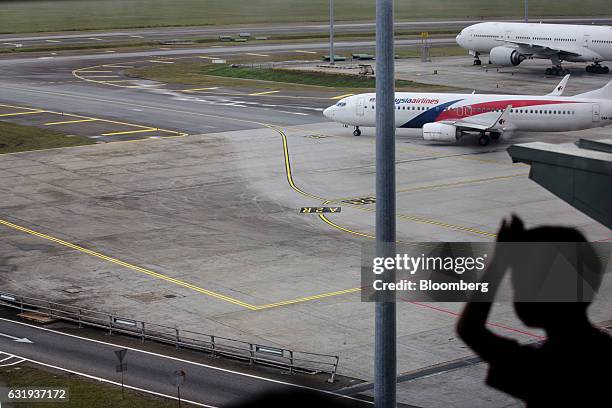 Boy looks out through a window as a Malaysian Airlines Bhd. Aircraft taxis on the tarmac at Kuala Lumpur International Airport in Sepang, Selangor,...