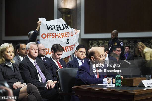 Billionaire investor Wilbur Ross, commerce secretary nominee for U.S. President-elect Donald Trump, pauses as protesters hold up a sign during a...