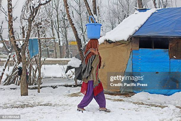 Girl ferrying water in buckets amid snow accumulated. Cold wave has gripped valley since past three weeks.