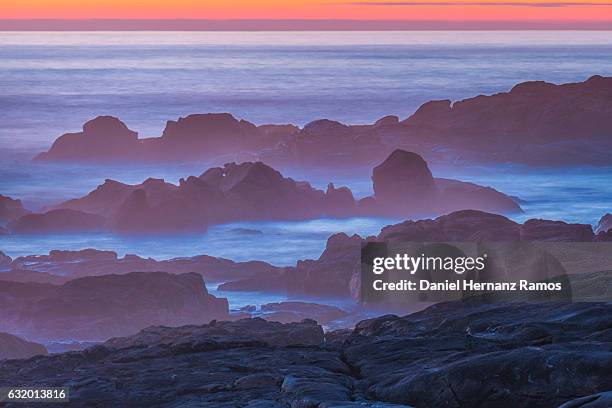 long exposure of rocky coastline with purple water and red sky. galicia - guarda sol stock pictures, royalty-free photos & images