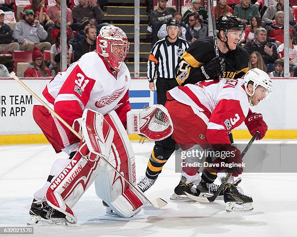 Jared Coreau of the Detroit Red Wings follows the play as teammate Nick Jensen battles for position with Riley Nash of the Boston Bruins during an...