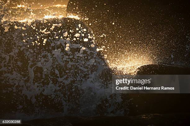 waves breaking against a rock close up illuminated by the setting sun - guarda sol stock pictures, royalty-free photos & images