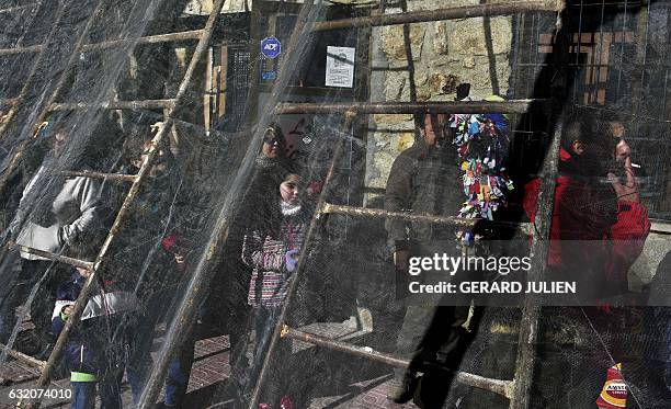 People shelter behind a net as they wait a man representing the Jarrampla to run through the streets beating a drum, in Piorna on January 19, 2017...