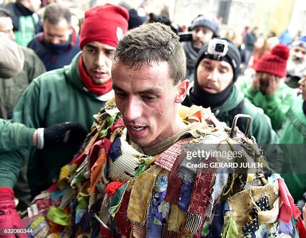 Man representing the Jarrampla without his mask, sporting a costume covered in multicoloured ribbons and his face hidden behind a conical mask with a...