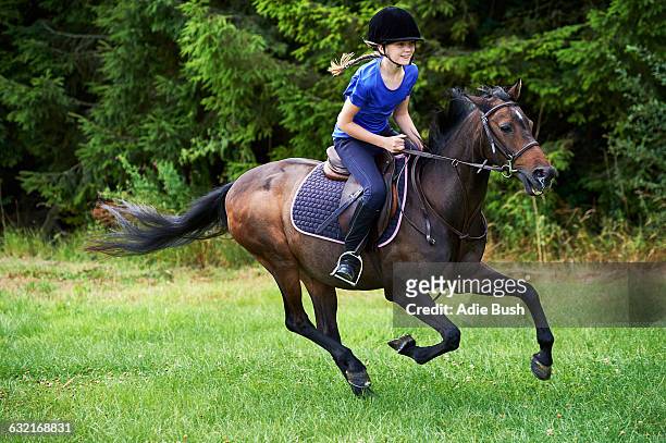 side view of girl wearing riding hat galloping on horseback - child horse stock pictures, royalty-free photos & images