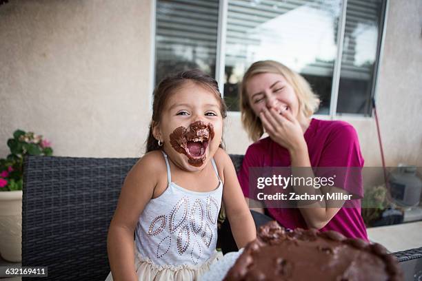 young girl, chocolate cake on her face, sitting with family member, laughing - kid birthday cake stock pictures, royalty-free photos & images