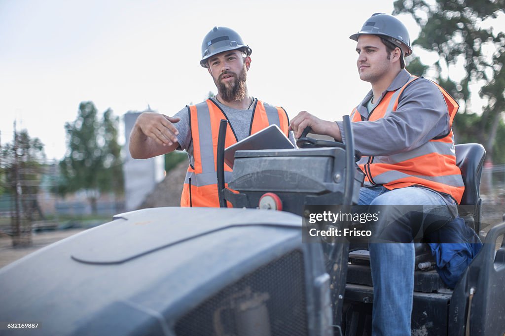 Site manager explaining to steamroller driver on construction site