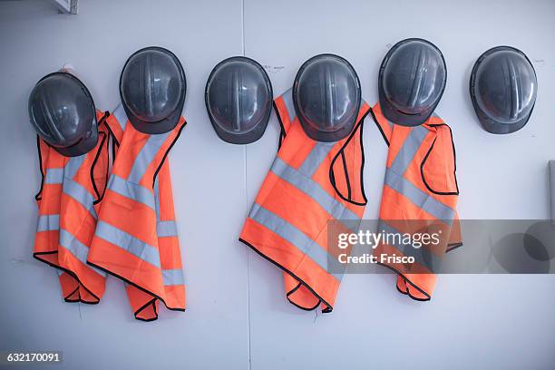 rows of hard hats and high vis jackets on portable cabin wall - protective workwear photos et images de collection