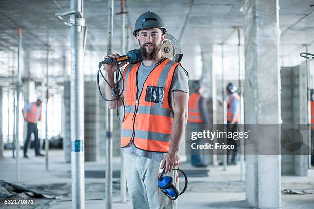 portrait of young male builder carrying circular saw on shoulder on construction site - elektrisch gereedschap stockfoto's en -beelden