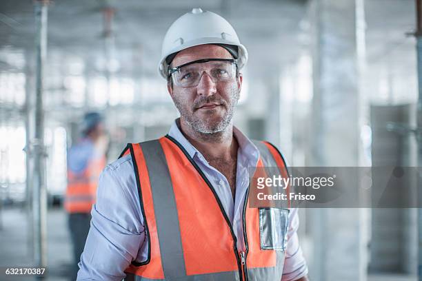 portrait of mid adult male site manager on construction site - ouvrier du bâtiment photos et images de collection