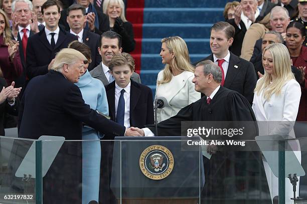 President Donald Trump shakes hands with Supreme Court Chief Justice John Roberts as his family looks on on the West Front of the U.S. Capitol on...