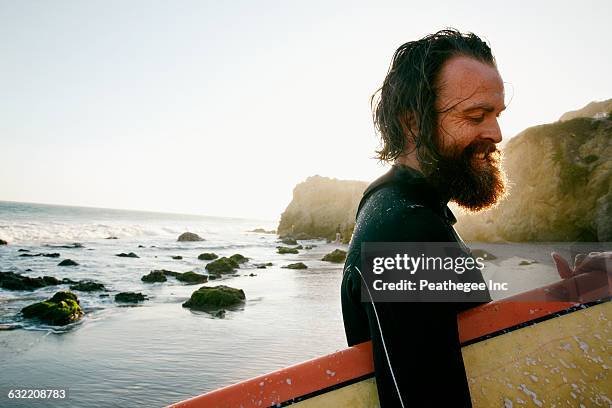 caucasian man holding surfboard at beach - surfbrett stock-fotos und bilder