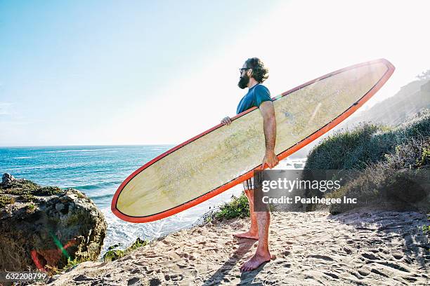 caucasian man holding surfboard at beach - active lifestyle los angeles stock pictures, royalty-free photos & images