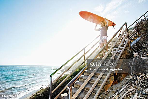 caucasian man carrying surfboard on stairs at beach - active lifestyle los angeles stock pictures, royalty-free photos & images