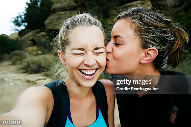 woman kissing cheek of friend outdoors - friends kissing cheeks fotografías e imágenes de stock